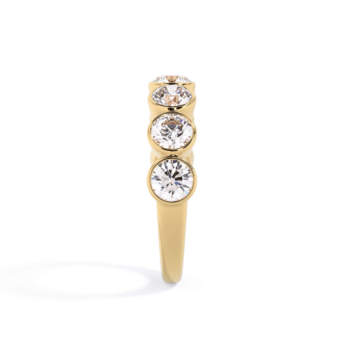 A picture of a seven stone diamond wedding ring with round diamonds that are bezel set in yellow gold on a white background with a side profile view.