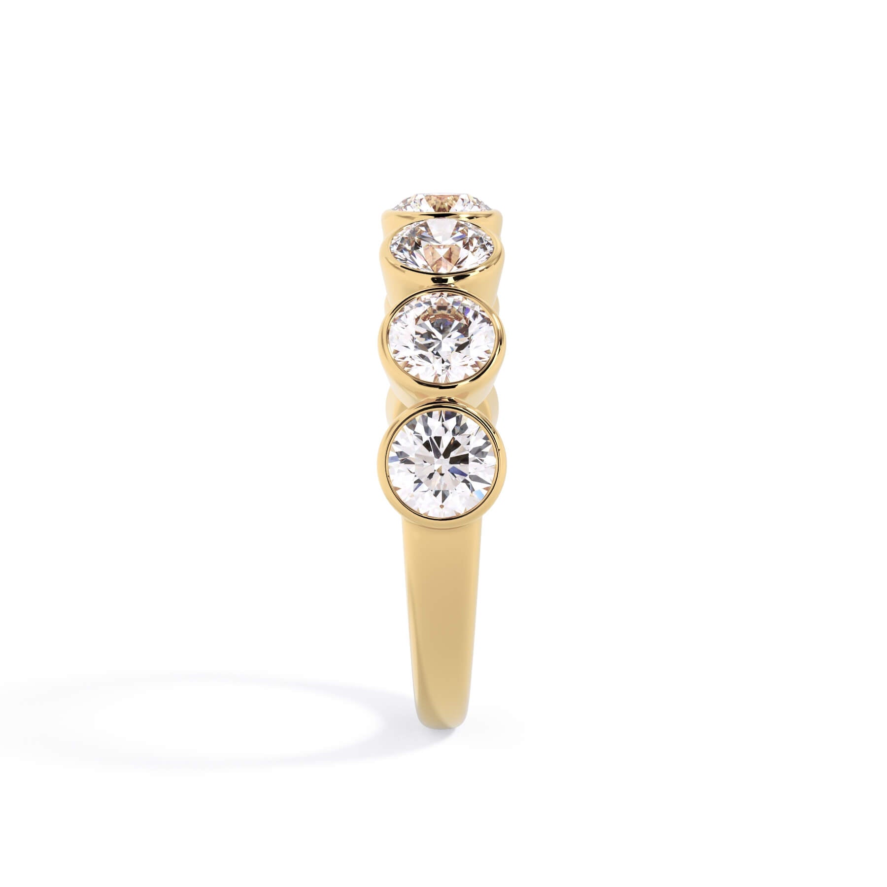 A picture of a seven stone diamond wedding ring with round diamonds that are bezel set in yellow gold on a white background with a side profile view.