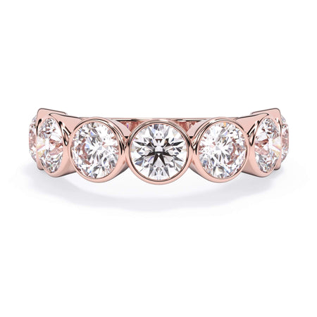 A picture of a seven stone diamond wedding ring with round diamonds that are bezel set in rose gold on a white background with the ring facing forward, lying down.