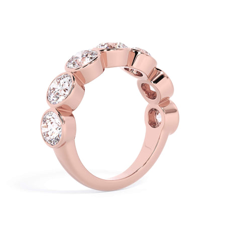 A picture of a seven stone diamond wedding ring with round diamonds that are bezel set in rose gold on a white background with a slightly angled, through the finger view.