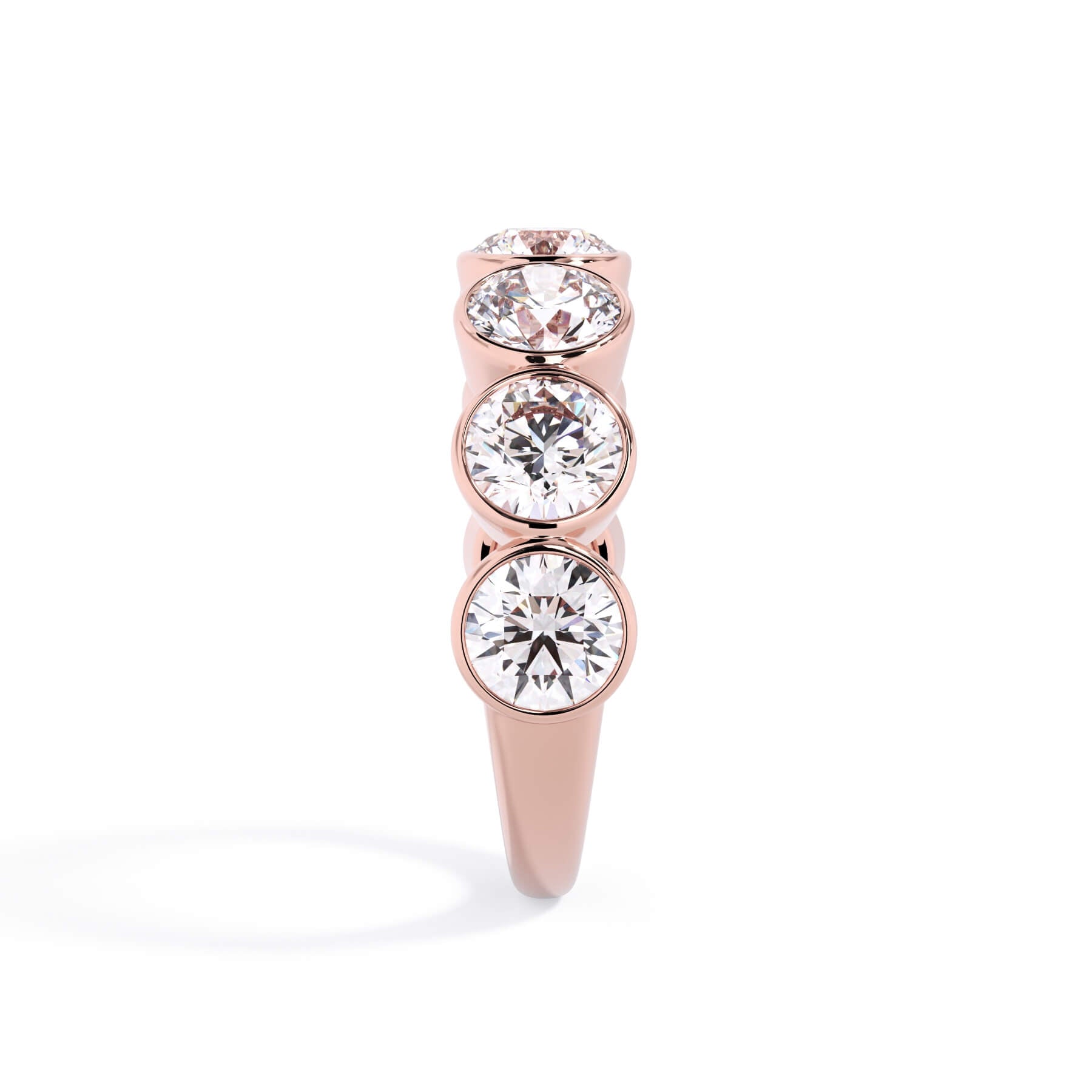 A picture of a seven stone diamond wedding ring with round diamonds that are bezel set in rose gold on a white background with a side profile view.