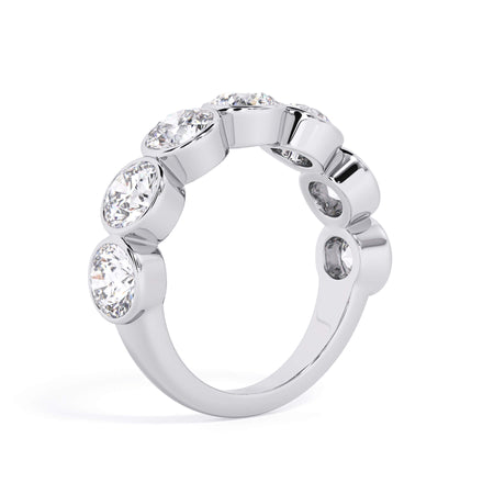 A picture of a seven stone diamond wedding ring with round diamonds that are bezel set in white gold or platinum on a white background with a slightly angled, through the finger view.