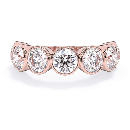 A picture of a seven stone diamond wedding ring with round diamonds that are bezel set in rose gold on a white background with the ring facing forward, lying down.