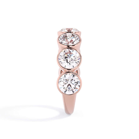 A picture of a seven stone diamond wedding ring with round diamonds that are bezel set in rose gold on a white background with a side profile view.