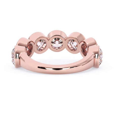 A picture of a seven stone diamond wedding ring with round diamonds that are bezel set in rose gold on a white background with a view of the underside of the ring.