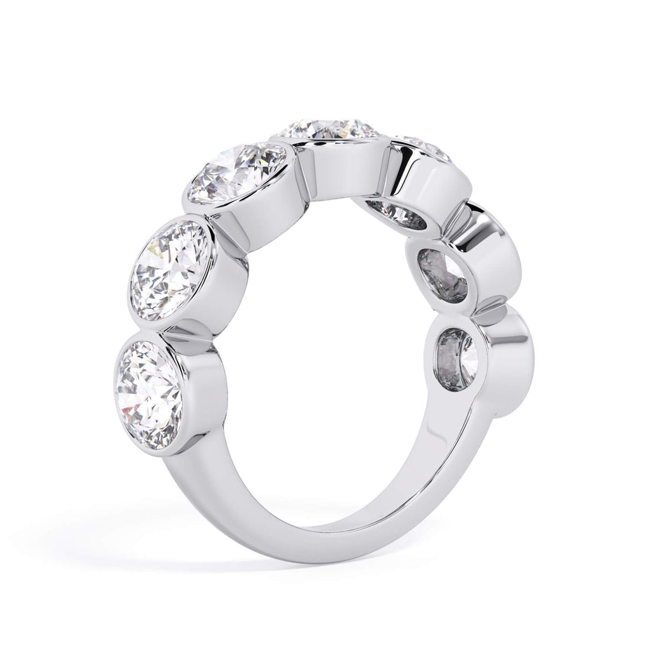 A picture of a seven stone diamond wedding ring with round diamonds that are bezel set in white gold or platinum on a white background with a slightly angled, through the finger view.