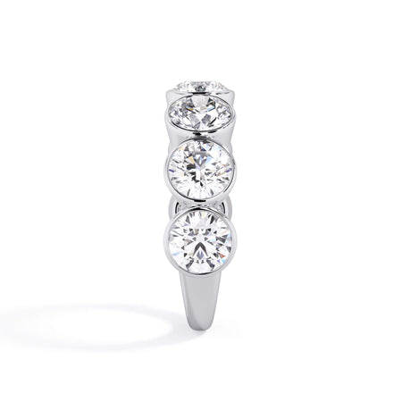 A picture of a seven stone diamond wedding ring with round diamonds that are bezel set in white gold or platinum on a white background with a side profile view.