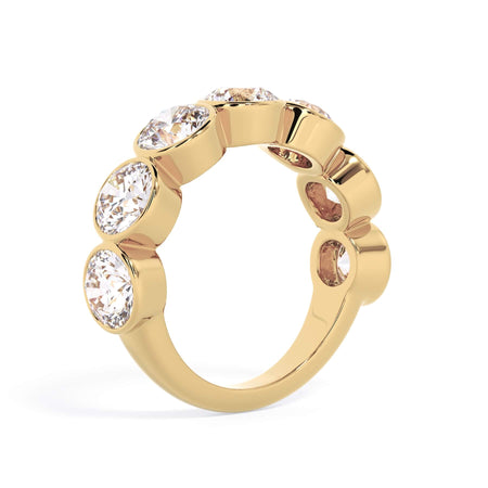 A picture of a seven stone diamond wedding ring with round diamonds that are bezel set in yellow gold on a white background with a slightly angled, through the finger view.