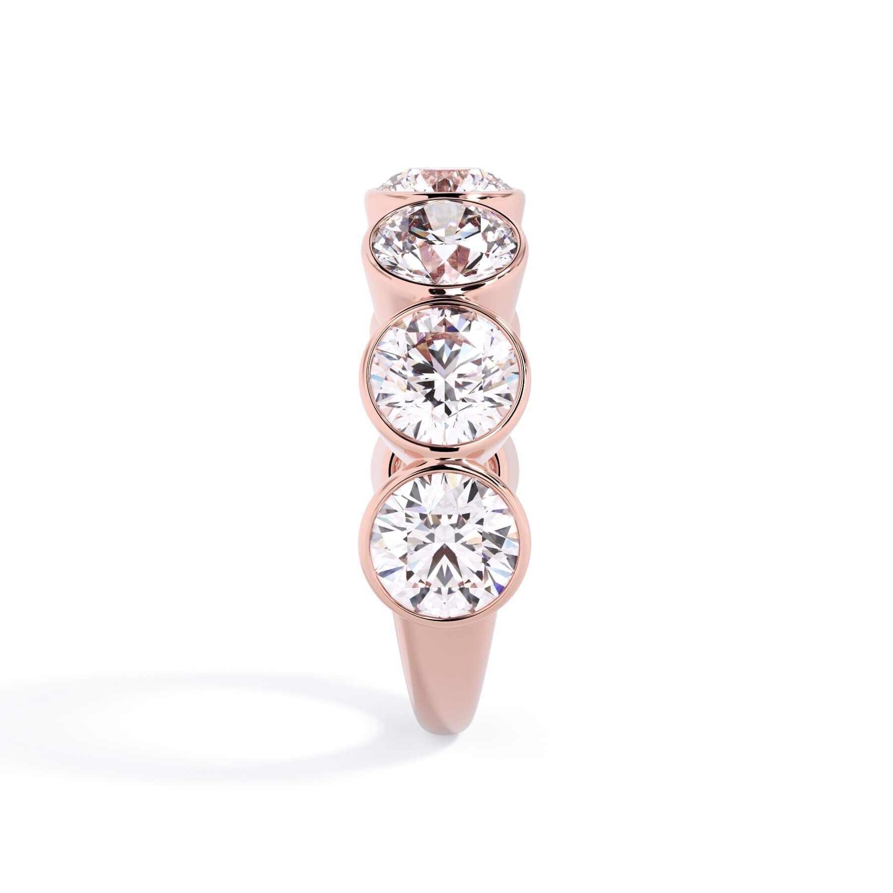 A picture of a seven stone diamond wedding ring with round diamonds that are bezel set in rose gold on a white background with a side profile view.
