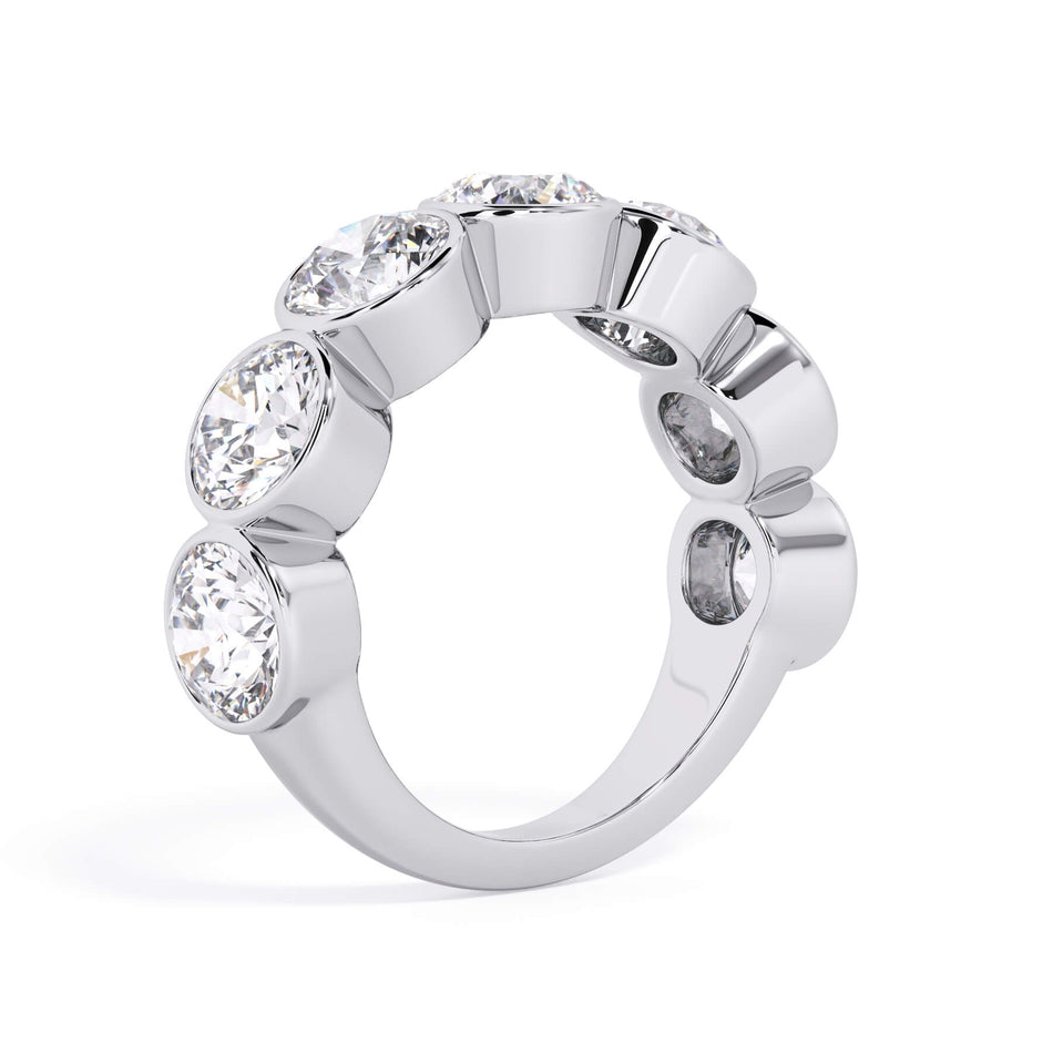 A picture of a seven stone diamond wedding ring with round diamonds that are bezel set in white gold or platinum on a white background with a slightly angled, through the finger view.
