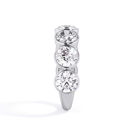 A picture of a seven stone diamond wedding ring with round diamonds that are bezel set in white gold or platinum on a white background with a side profile view.