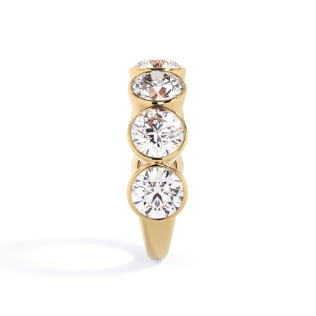 A picture of a seven stone diamond wedding ring with round diamonds that are bezel set in yellow gold on a white background with a side profile view.