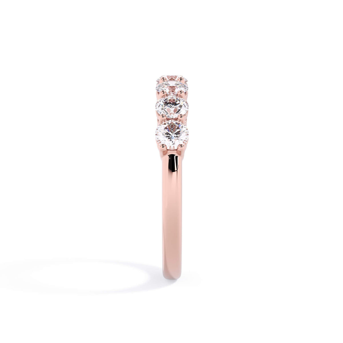 A picture of a seven stone diamond wedding ring with round diamonds that are shared prong set in rose gold on a white background with a side profile view.