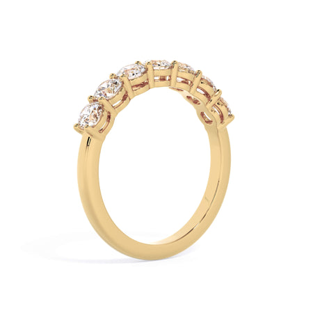 A picture of a seven stone diamond wedding ring with round diamonds that are shared prong set in yellow gold on a white background with a slightly angled, through the finger view.