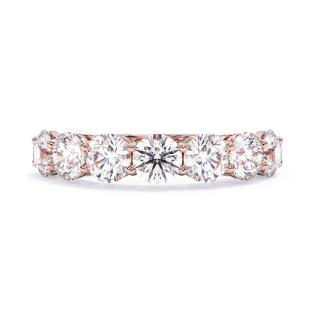 A picture of a seven stone diamond wedding ring with round diamonds that are shared prong set in rose gold on a white background with the ring facing forward, lying down.