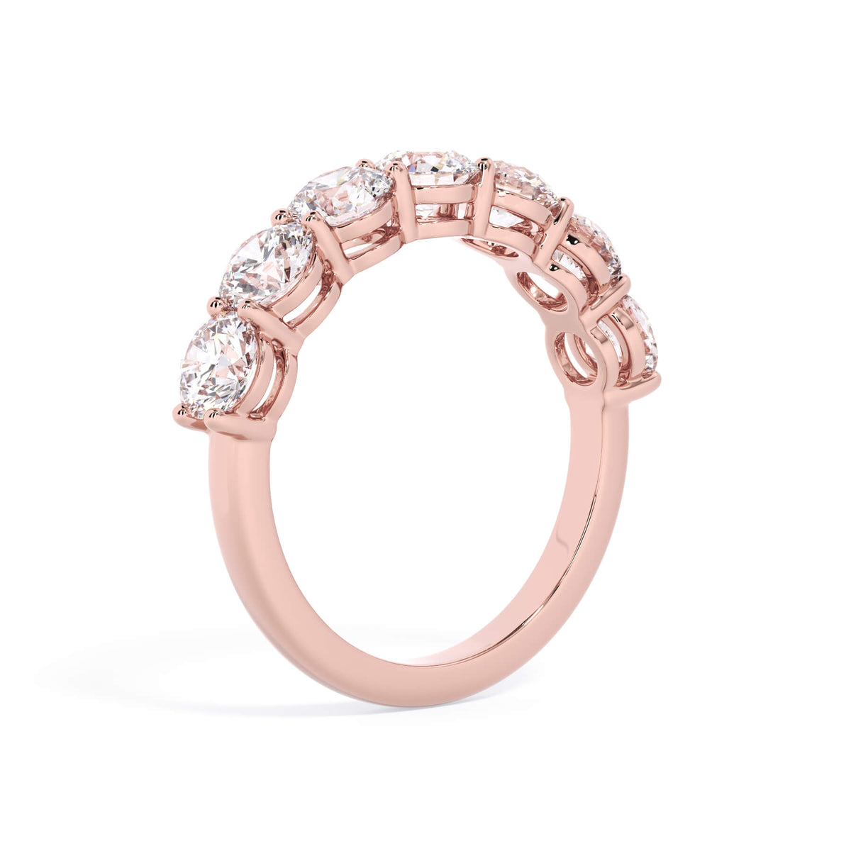 A picture of a seven stone diamond wedding ring with round diamonds that are shared prong set in rose gold on a white background with a slightly angled, through the finger view.