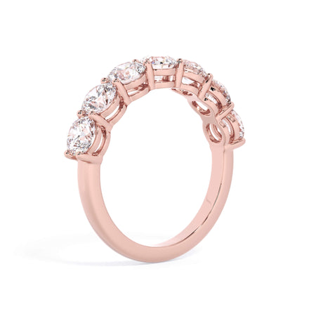 A picture of a seven stone diamond wedding ring with round diamonds that are shared prong set in rose gold on a white background with a slightly angled, through the finger view.
