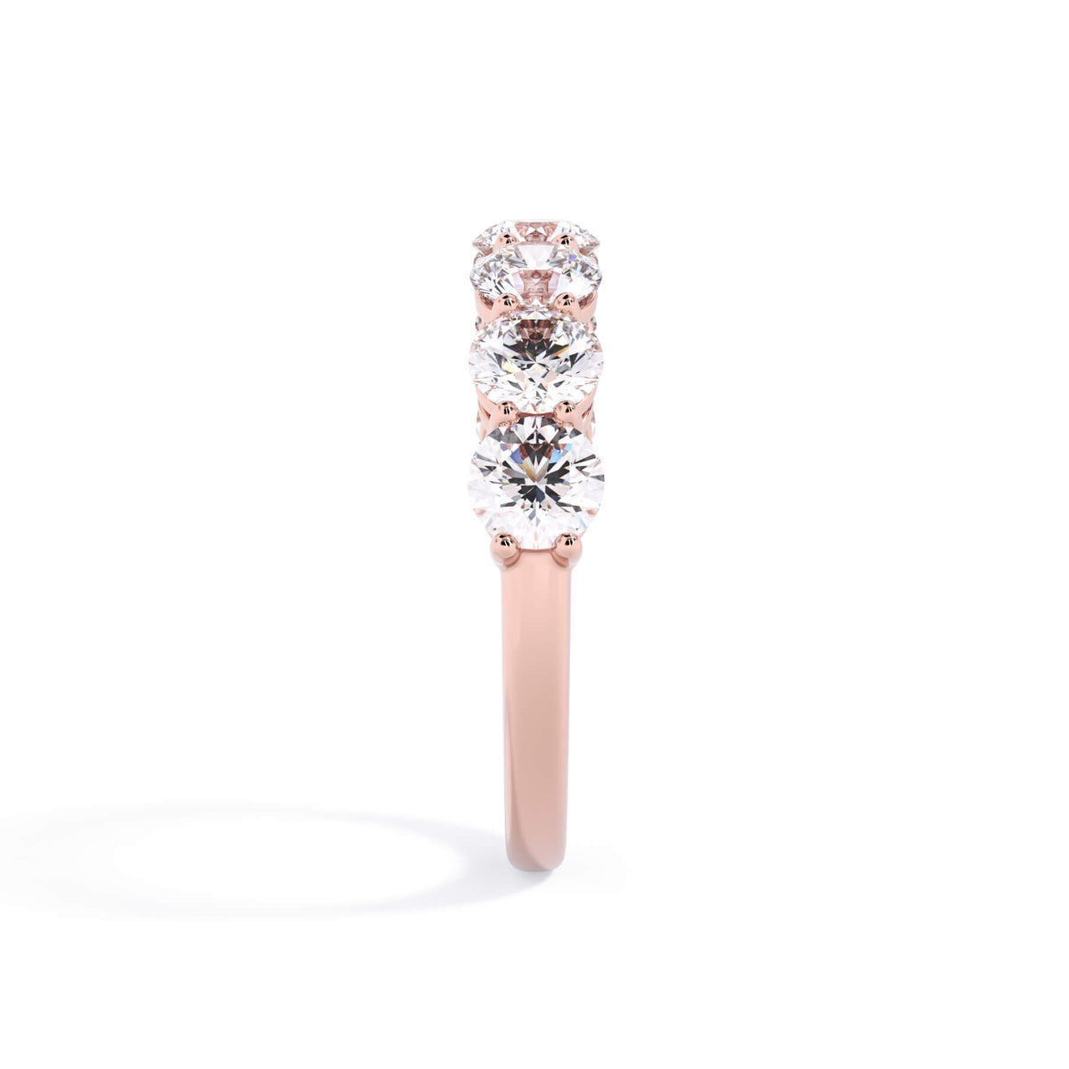 A picture of a seven stone diamond wedding ring with round diamonds that are shared prong set in rose gold on a white background with a side profile view.