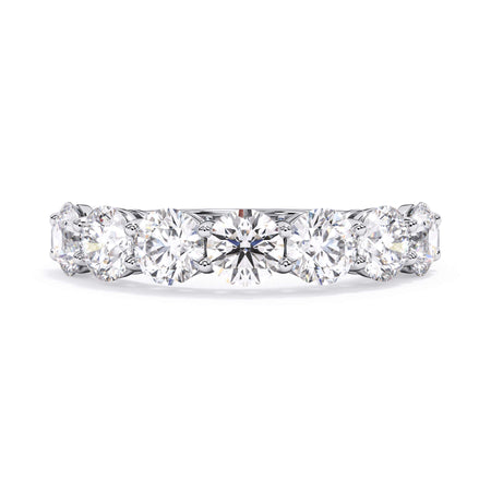 A picture of a seven stone diamond wedding ring with round diamonds that are shared prong set in white gold or platinum on a white background with the ring facing forward, lying down.