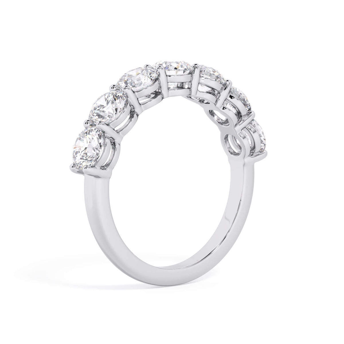 A picture of a seven stone diamond wedding ring with round diamonds that are shared prong set in white gold or platinum on a white background with a slightly angled, through the finger view.