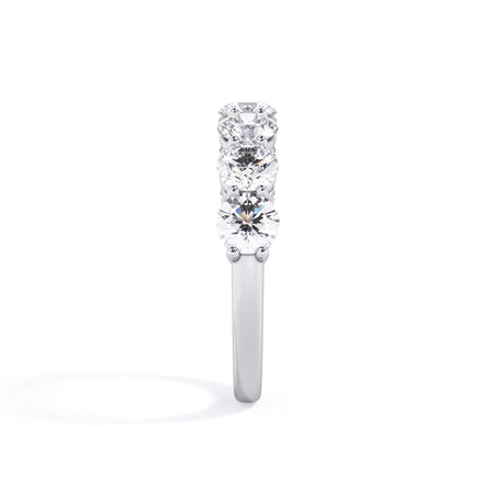 A picture of a seven stone diamond wedding ring with round diamonds that are shared prong set in white gold or platinum on a white background with a side profile view.