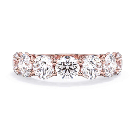 A picture of a seven stone diamond wedding ring with round diamonds that are shared prong set in rose gold on a white background with the ring facing forward, lying down.