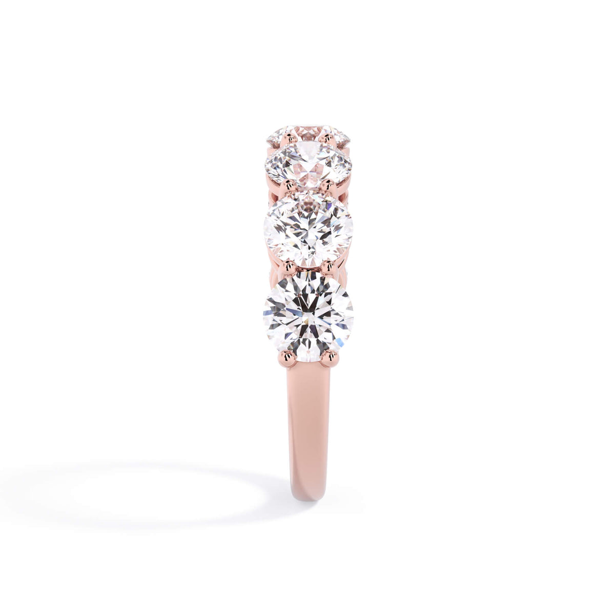 A picture of a seven stone diamond wedding ring with round diamonds that are shared prong set in rose gold on a white background with a side profile view.