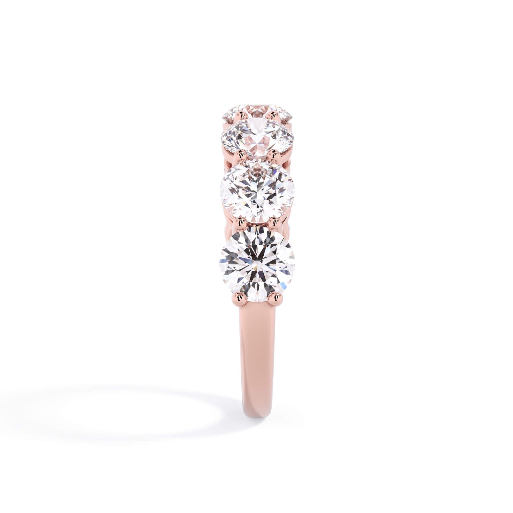 A picture of a seven stone diamond wedding ring with round diamonds that are shared prong set in rose gold on a white background with a side profile view.