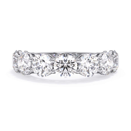 A picture of a seven stone diamond wedding ring with round diamonds that are shared prong set in white gold or platinum on a white background with the ring facing forward, lying down.
