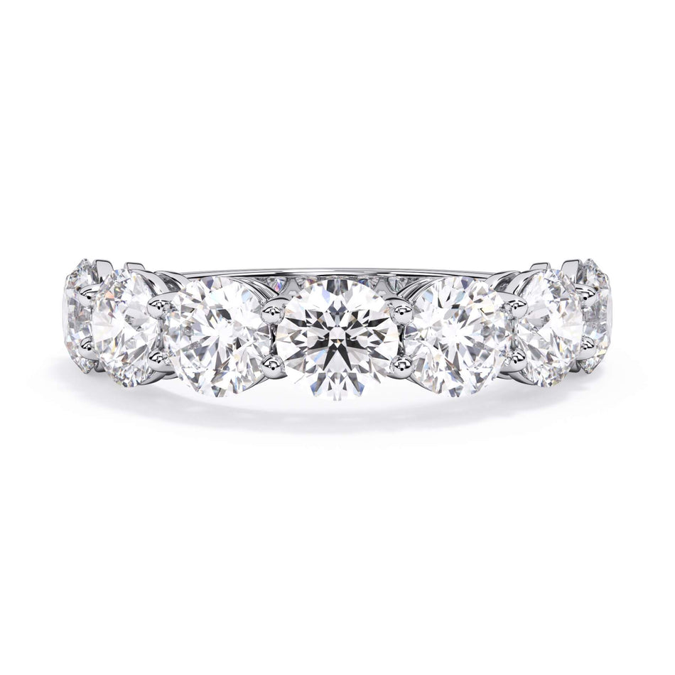 A picture of a seven stone diamond wedding ring with round diamonds that are shared prong set in white gold or platinum on a white background with the ring facing forward, lying down.
