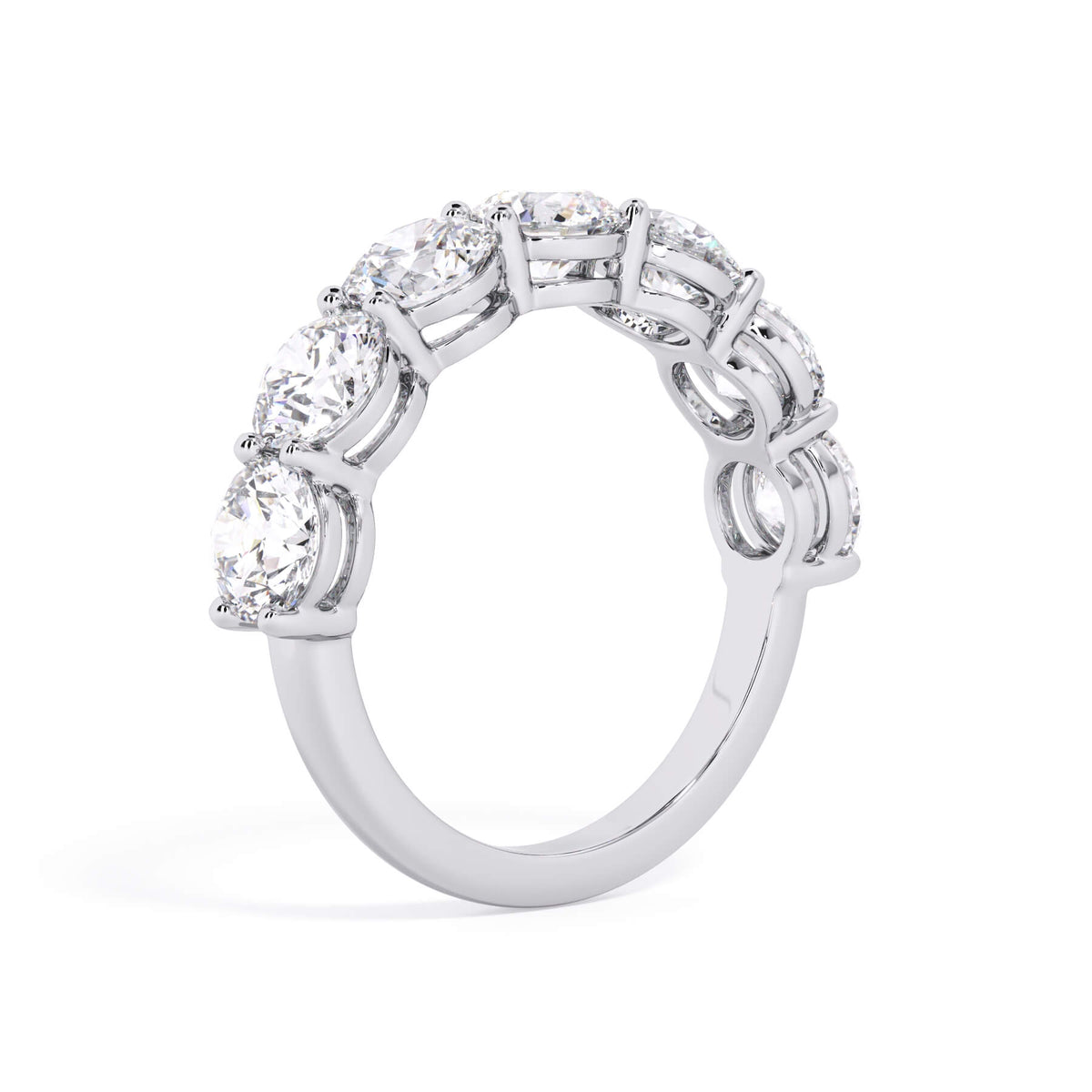 A picture of a seven stone diamond wedding ring with round diamonds that are shared prong set in white gold or platinum on a white background with a slightly angled, through the finger view.