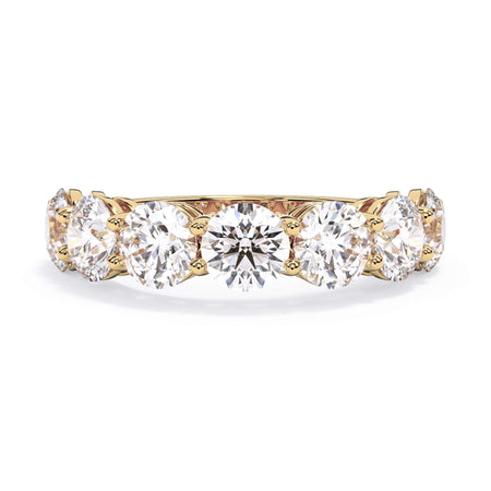 A picture of a seven stone diamond wedding ring with round diamonds that are shared prong set in yellow gold on a white background with the ring facing forward, lying down.