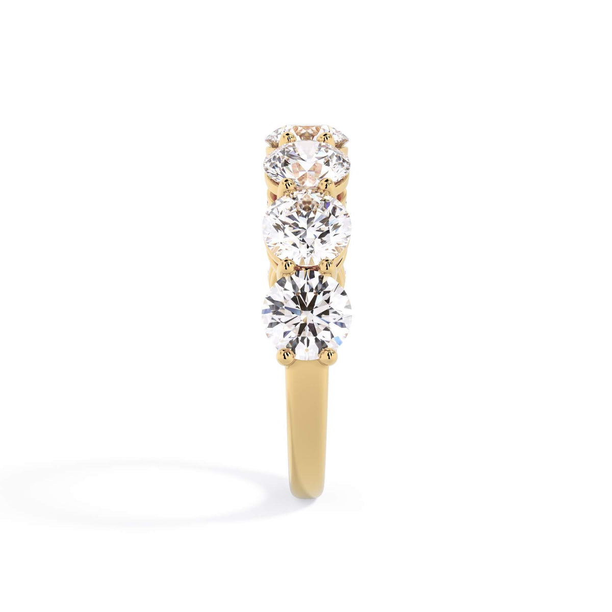 A picture of a seven stone diamond wedding ring with round diamonds that are shared prong set in yellow gold on a white background with a side profile view.