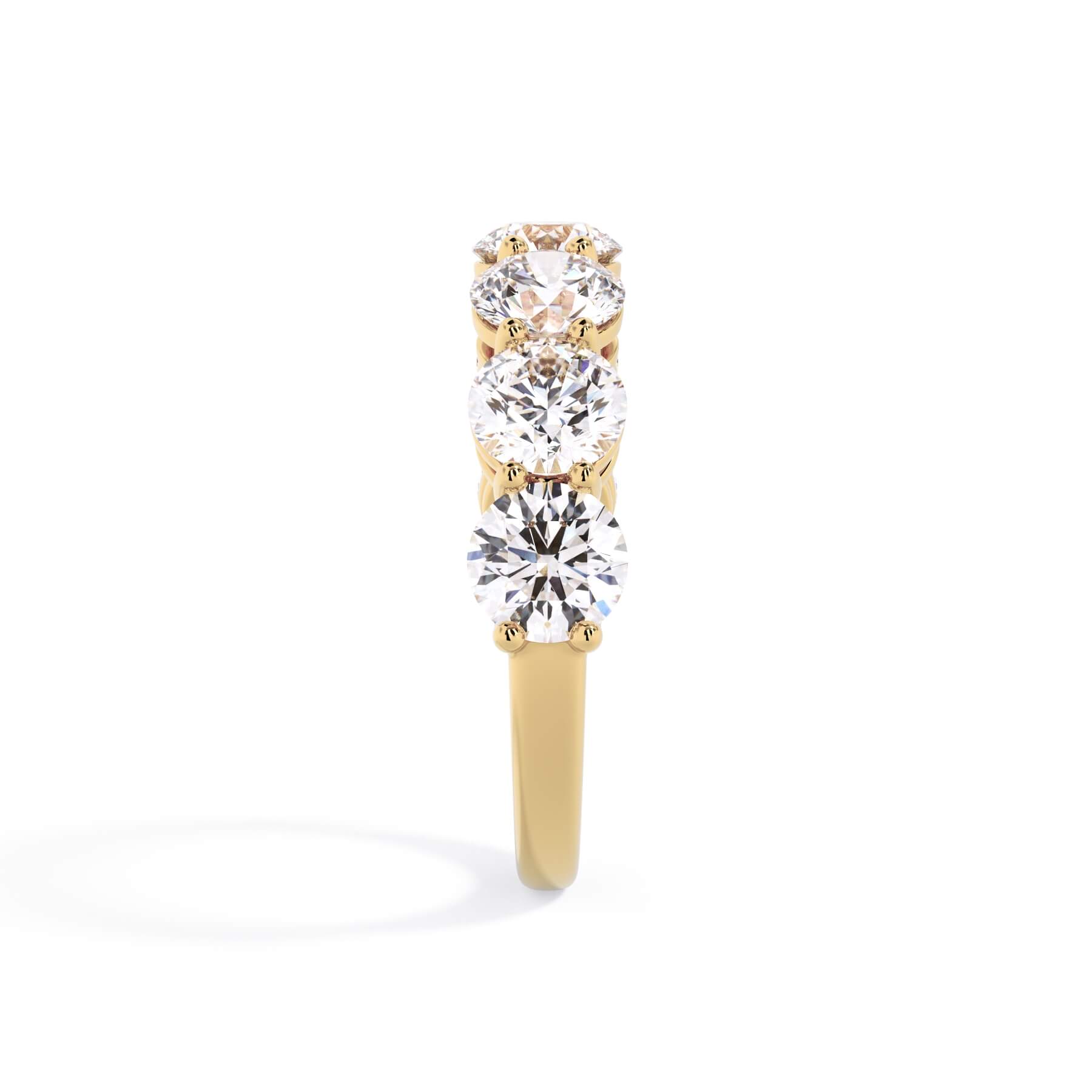 A picture of a seven stone diamond wedding ring with round diamonds that are shared prong set in yellow gold on a white background with a side profile view.