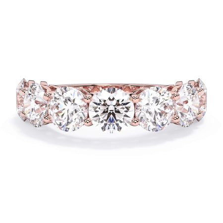 A picture of a seven stone diamond wedding ring with round diamonds that are shared prong set in rose gold on a white background with the ring facing forward, lying down.