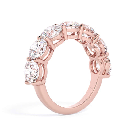 A picture of a seven stone diamond wedding ring with round diamonds that are shared prong set in rose gold on a white background with a slightly angled, through the finger view.