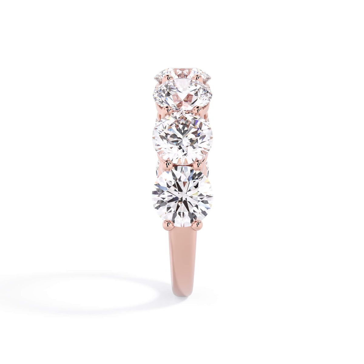 A picture of a seven stone diamond wedding ring with round diamonds that are shared prong set in rose gold on a white background with a side profile view.