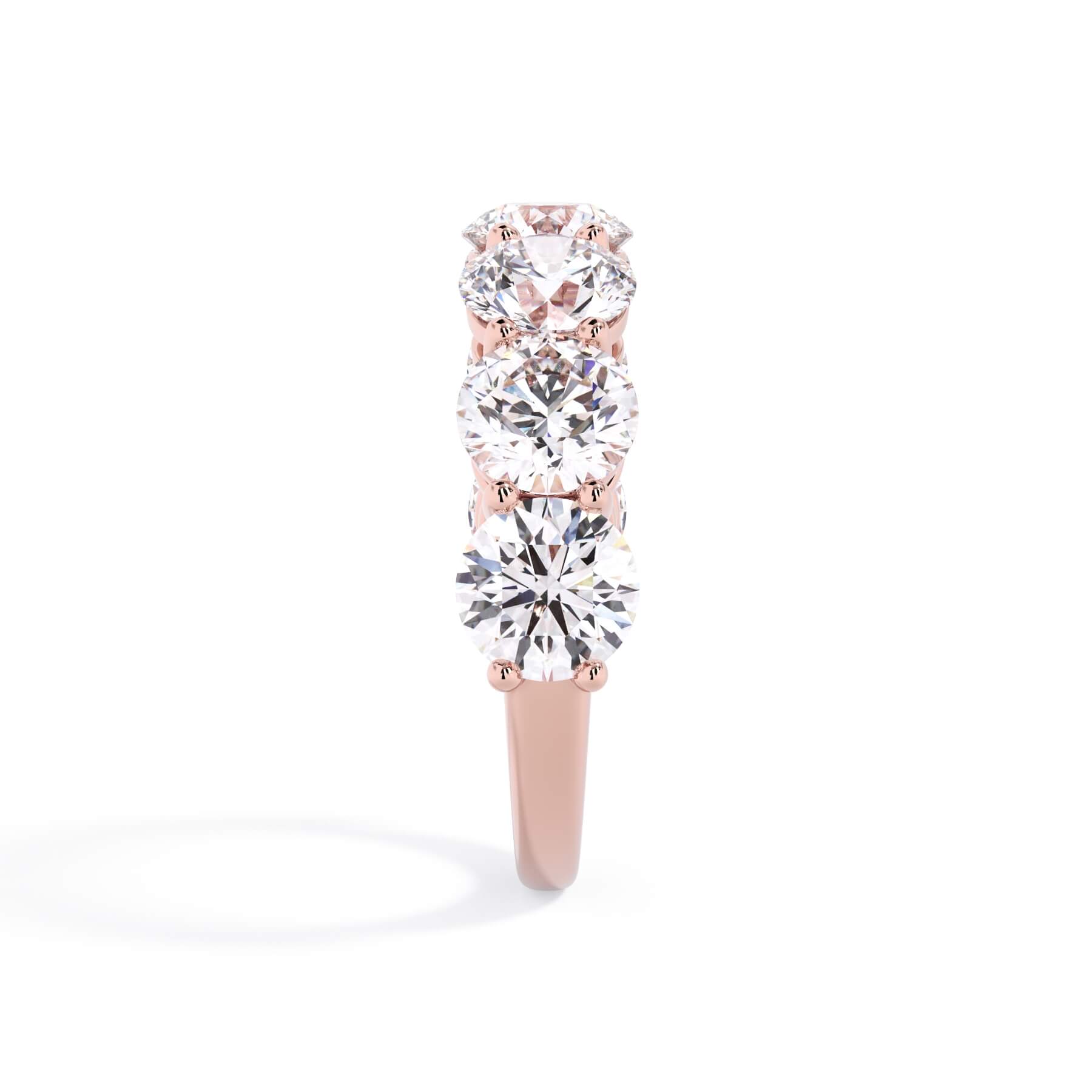 A picture of a seven stone diamond wedding ring with round diamonds that are shared prong set in rose gold on a white background with a side profile view.