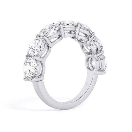 A picture of a seven stone diamond wedding ring with round diamonds that are shared prong set in white gold or platinum on a white background with a slightly angled, through the finger view.