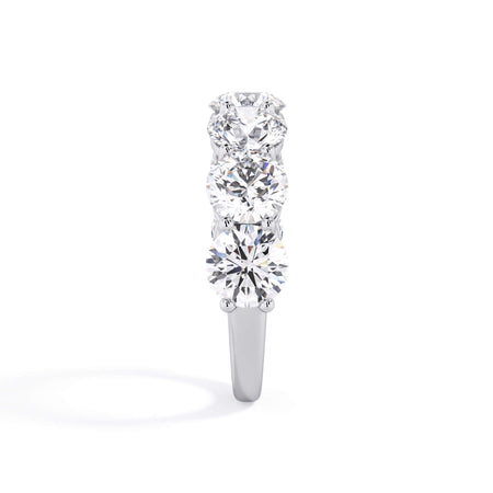 A picture of a seven stone diamond wedding ring with round diamonds that are shared prong set in white gold or platinum on a white background with a side profile view.