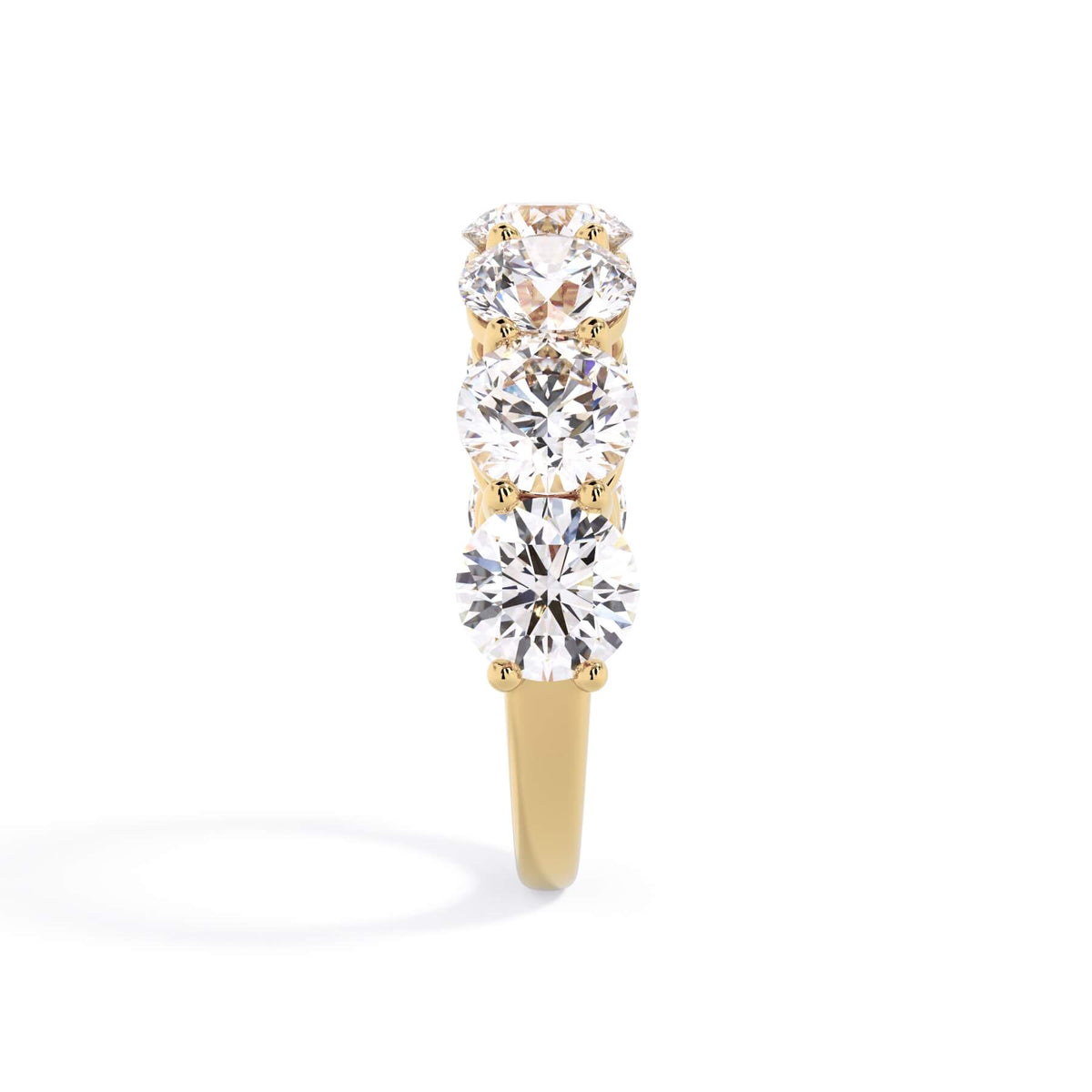 A picture of a seven stone diamond wedding ring with round diamonds that are shared prong set in yellow gold on a white background with a side profile view.