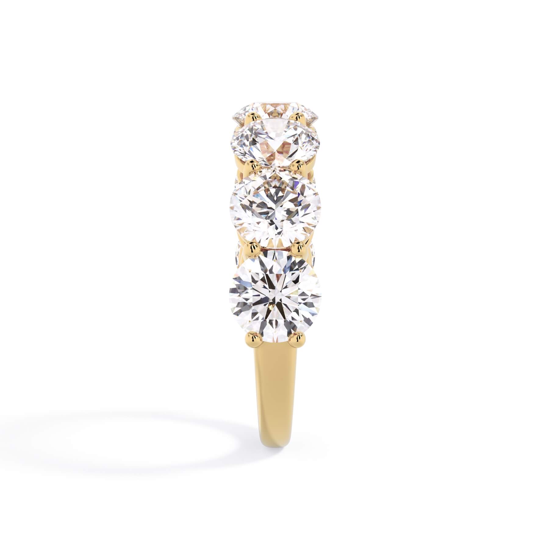 A picture of a seven stone diamond wedding ring with round diamonds that are shared prong set in yellow gold on a white background with a side profile view.