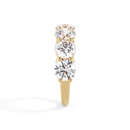 A picture of a seven stone diamond wedding ring with round diamonds that are shared prong set in yellow gold on a white background with a side profile view.
