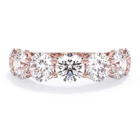 A picture of a seven stone diamond wedding ring with round diamonds that are shared prong set in rose gold on a white background with the ring facing forward, lying down.