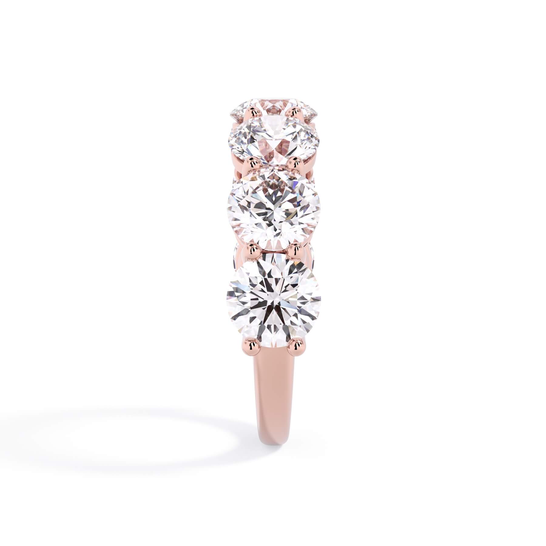 A picture of a seven stone diamond wedding ring with round diamonds that are shared prong set in rose gold on a white background with a side profile view.
