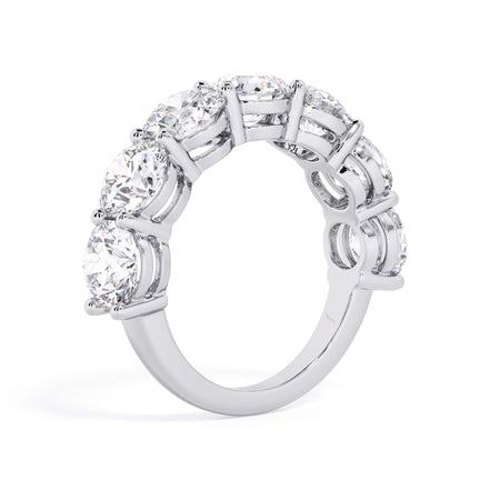 A picture of a seven stone diamond wedding ring with round diamonds that are shared prong set in white gold or platinum on a white background with a slightly angled, through the finger view.