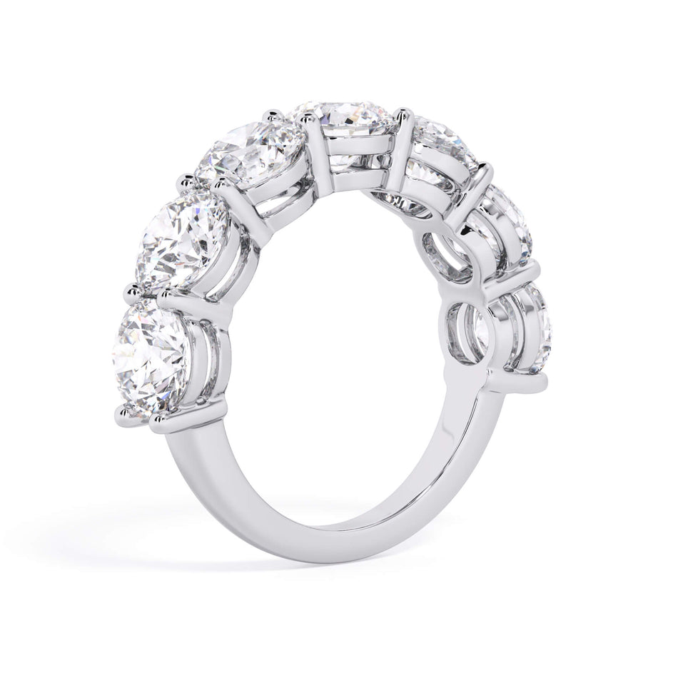 A picture of a seven stone diamond wedding ring with round diamonds that are shared prong set in white gold or platinum on a white background with a slightly angled, through the finger view.