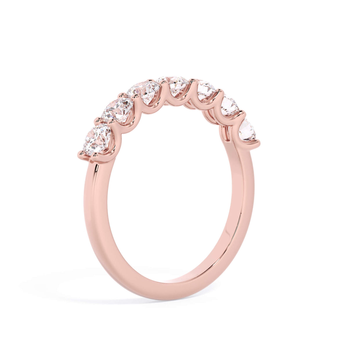 A picture of a seven stone diamond wedding ring with round diamonds that are U prong set in rose gold on a white background with a slightly angled, through the finger view.