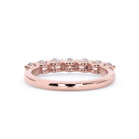 A picture of a seven stone diamond wedding ring with round diamonds that are U prong set in rose gold on a white background with a view of the underside of the ring.
