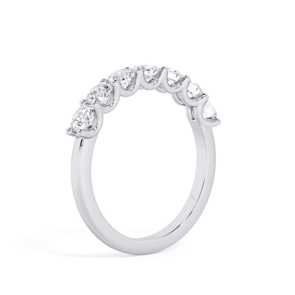 A picture of a seven stone diamond wedding ring with round diamonds that are U prong set in white gold or platinum on a white background with a slightly angled, through the finger view.